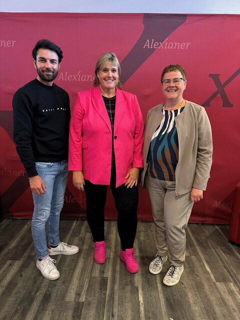 Drei Personen stehen vor einem roten Hintergrund mit dem Wort "Alexianer" und einem "X".