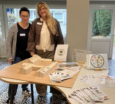 Mareike Gördemann und Carolin Amthor-Bröker präsentieren auf einem Tisch ein Holzmodell des Kolping Gutshofs